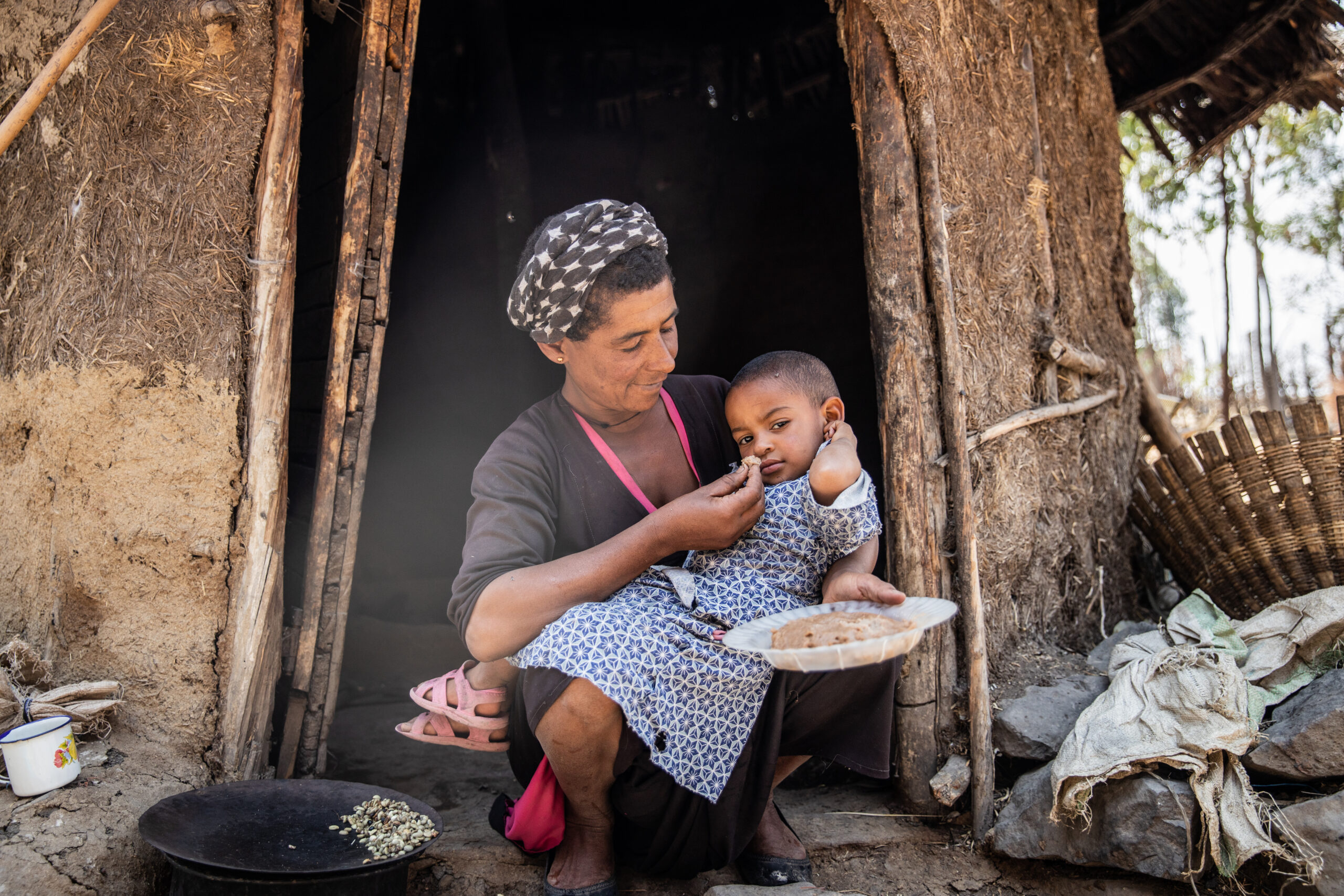 A mother feeds her young child outside their home in rural Ethiopia